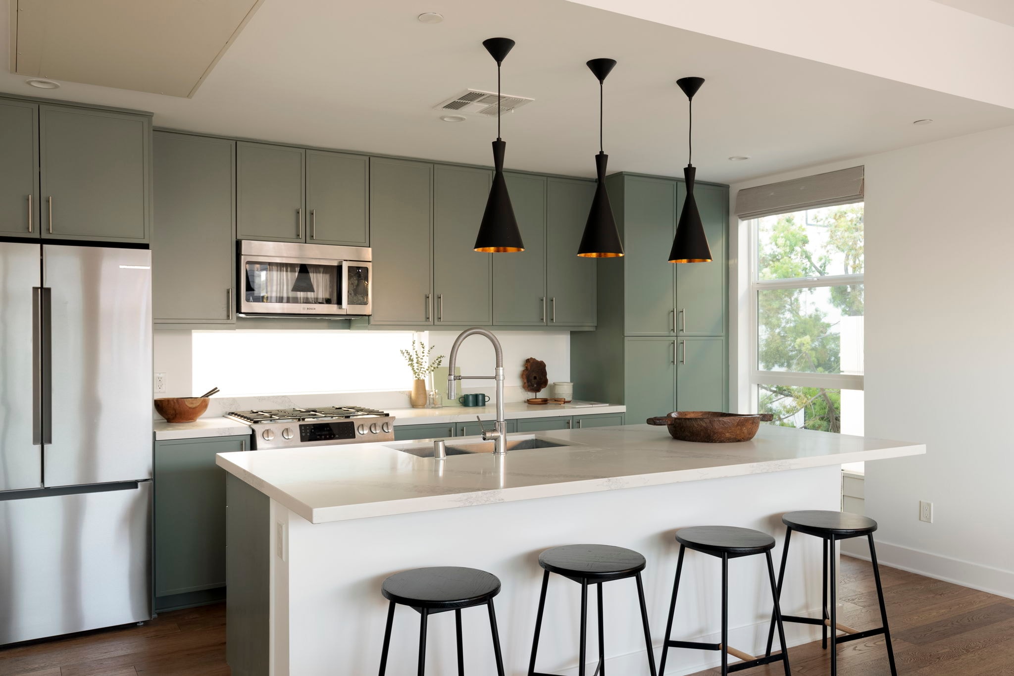 Modern kitchen with sage green cabinetry and black pendant lights